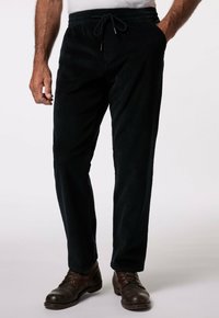 Pantalons en velours côtelé noirs avec une taille à cordon de serrage, deux poches latérales et une finition texturée douce. Portés avec des chaussures en cuir marron.