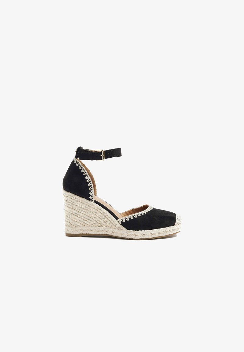 Espadrille compensée noire avec boucle à la bride de cheville et détails de couture blanche sur la semelle en jute et autour des zones des orteils et du talon.