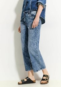 Lichtblauwe denim cropped jeans met een ontspannen pasvorm en vervaagde textuur, gecombineerd met zwarte sandalen met gouden gespen en kurken zolen.