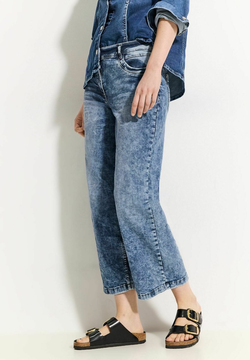 Lichtblauwe denim cropped jeans met een ontspannen pasvorm en vervaagde textuur, gecombineerd met zwarte sandalen met gouden gespen en kurken zolen.