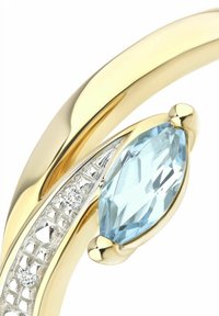 Zlatý prsteň s modrým kameňom brúseným do tvaru marquise, obklopený textúrovaným strieborným pásikom s malými priehľadnými akcentmi. Hladký a leštený povrch.