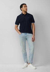 Navy polo shirt with turquoise accents and short sleeves, paired with light blue jeans and white sneakers. Simple design and casual fit.