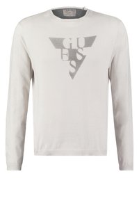 Biały sweter z długim rękawem wykonany z miękkiego materiału, z szarym trójkątnym logo z napisem "GUESS" w stylizowanych literach na środku.