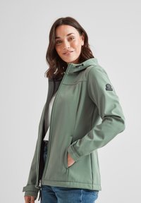 Green softshell jacket with a zippered front, hood, and side pockets. Features a smooth texture and embroidered logo on the sleeve.