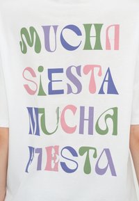 Бяла риза с цветен, стилизиран текст, който гласи "MUCHA SIESTA MUCHA FIESTA" в зелени, лилави, розови и сини букви.