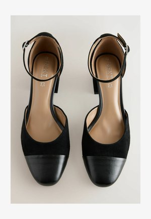 Chaussures à talons hauts noires avec une finition en daim, dotées d'une bride de cheville et d'un bout arrondi, sur un fond neutre.