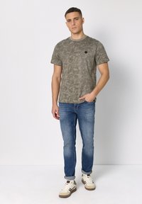 Olivově zelené tričko s krátkými rukávy, kulatým výstřihem a malým černým logem. Doplněné světlomodrými džínami a bílými teniskami.