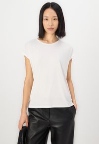 Weißes kurzärmliges T-Shirt mit rundem Ausschnitt und lockerer Passform, aus einem weichen Material gefertigt. Kombiniert mit schwarzen Lederhosen.