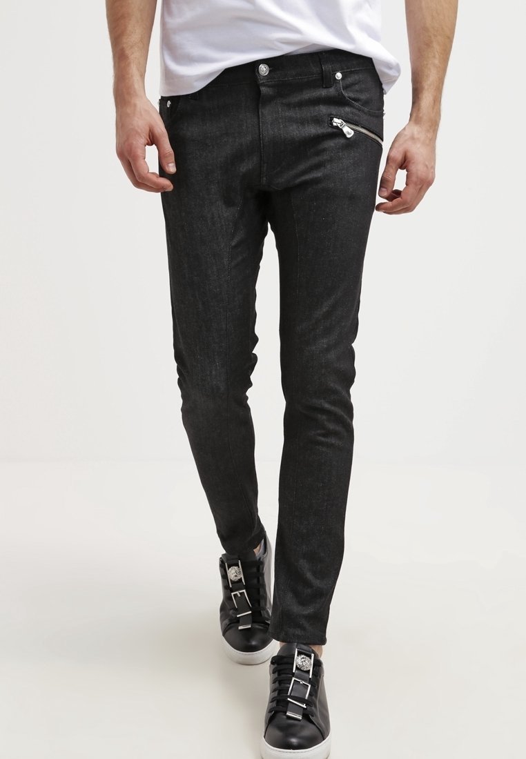 Homme portant un jean noir slim avec une poche zippée en diagonale et des baskets noires aux semelles blanches, marchant vers l'avant.