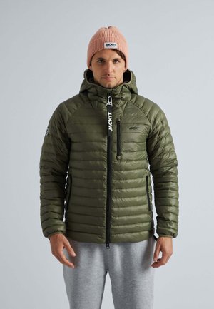 Giacca puffer verde oliva con cappuccio, texture trapuntata, zip nera e dettagli con logo; indossata sopra pantaloni della tuta grigi e un berretto di maglia rosa.