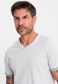 V-hals T-shirt i lysegrå med korte ærmer med grå detaljer; struktureret stof med afslappet pasform; rent, minimalistisk design.