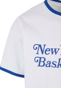 Hvit bomull T-skjorte med korte ermer, med blå ribbestrikket krage og kant på ermene; trykt tekst leser "New York Basketball" i blått.
