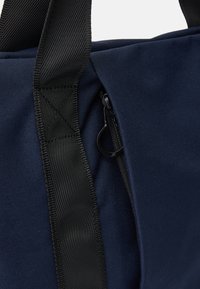 Marineblaue Tragetasche aus robustem Stoff, mit einem schwarzen Reißverschluss und Webriemen. Eine Nahaufnahme zeigt die Textur und Nähdetails.