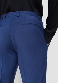 Blaue maßgeschneiderte Hosen mit glatter Textur, schlankem Schnitt und zwei Gesäßtaschen. Das Material wirkt leicht und eignet sich gut für smarte Freizeitkleidung.