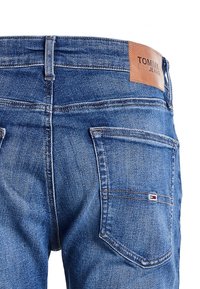 Tummansiniset farkut, joissa on ruskea nahkainen logo-patch, näkyvät ompeleet ja kaksi takataskua, joissa on pieni brändin emblem.