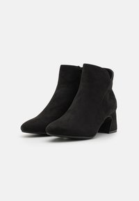 Botines de ante negros, con punta afilada y tacón bloque de altura media. Cuentan con una cremallera lateral para mayor comodidad al ponérselos. Textura suave, diseño minimalista.