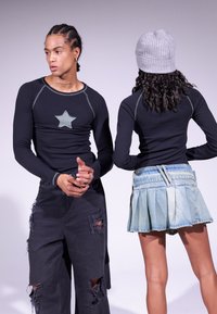 Cămașă neagră cu mânecă lungă, detaliu cu stea gri, asortată cu pantaloni negri rupți. Modelul mai poartă o beretă gri cu model în relief și o fustă din denim plisată.