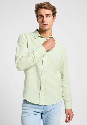 Hellgrünes Hemd mit Knopfleiste, aus strukturiertem Stoff, mit spitzem Kragen, langen Ärmeln und abgerundetem Saum. Dazu hellblaue Jeans getragen.
