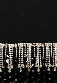 Tissu noir avec une frange perlée, comprenant des fils décoratifs argentés et des paillettes. La texture est lisse avec des accents brillants.