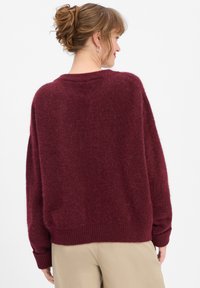 Maroon knitted sweater with a loose fit, ribbed cuffs and hem, and a soft texture, featuring a crew neckline and dropped shoulders.