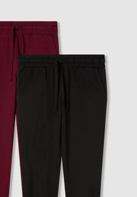 Dwie pary spodni dresowych: jedna bordowa, a druga czarna, obie z elastycznym pasem, sznurkiem w talii i bocznymi kieszeniami. Gładki bawełniany materiał.