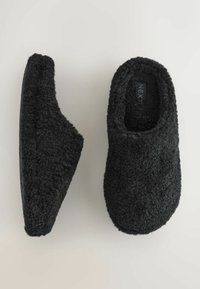 Papuci negri din blană falsă moale, cu spatele închis, vârful rotunjit și talpă din cauciuc texturată pentru aderență.