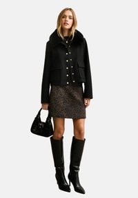 Czarna krótka kurtka z futrzanym kołnierzem, złotymi guzikami, zestawiona ze spódnicą w panterkę, czarnymi kozakiami do kolan oraz małą czarną torebką.