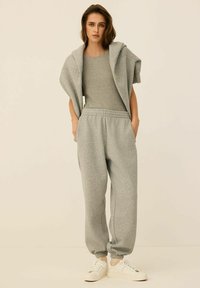 Szary bawełniany zestaw: bluza z kapturem i dresy. Bluza ma kaptur, a dresy posiadają elastyczny pas i mankiety. Uzupełnione białymi sneakersami.