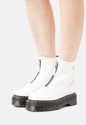 Bottines blanches en cuir avec des zips noirs et une semelle épaisse noire. Caractéristiques de coutures orange et d'un fond texturé et robuste.