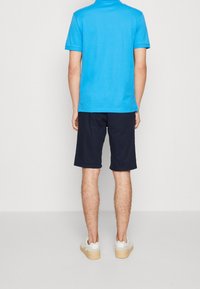 Polo de manga corta azul brillante, pantalones cortos navy y zapatillas blancas. El material parece suave; la camisa tiene un cuello clásico y un corte relajado.