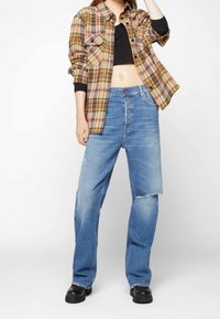 Rutigt flanellskjorta i beige, rosa och svart med två bröstfickor; ihop med ljusblå slitna jeans och svarta platåstövlar.