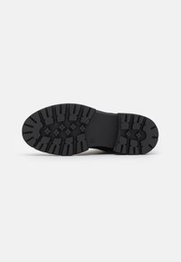 Suela de bota de goma negra con surcos profundos y patrones hexagonales para tracción. Textura lisa con diseño de punta redondeada y talón reforzado.