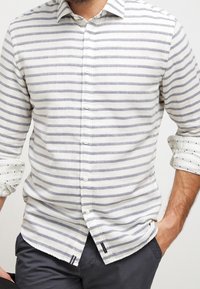 Camicia con colletto e bottini realizzata in un tessuto leggero, caratterizzata da righe orizzontali grigie e bianche, con maniche arrotolate e accenti discreti.