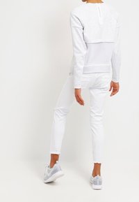 Grå sweatshirt med dragkedja bak, lager-på-lager över en vit topp. Vita slitna skinny jeans och gråa sportskor kompletterar outfiten.