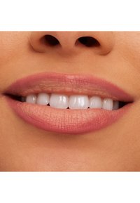 Nærbilde av lepper med en matt rosa finish, som viser hvite tenner og glatt hudstruktur rundt munnen. Ingen synlige sminkefeil.