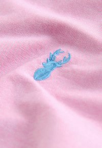 Rosa Stoff mit einem strukturierten Muster, das ein kleines blaues gesticktes Hirschdesign zeigt und das weiche Material sowie die detaillierte Stickerei hervorhebt.