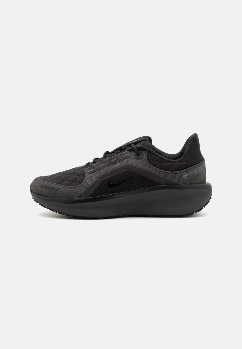 Chaussure de sport noire avec un dessus en tissu matelassé texturé, au design épuré, et semelle en caoutchouc noir. Présente un logo visible et une marque Gore-Tex.