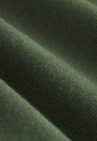 Gros plan d'un tissu vert olive texturé avec des motifs tricotés visibles et des motifs tissés doux formant de légers plis.
