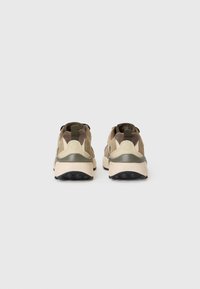 Zapatillas que presentan una combinación de tela en tonos beige y verde oliva, con un diseño texturizado, refuerzo en el talón y suela de goma de contraste.