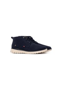 Botas de tobillo de ante azul marino con suela de goma beige, con diseño de cordones y pequeño logo en el lateral. Textura suave, forma aerodinámica.