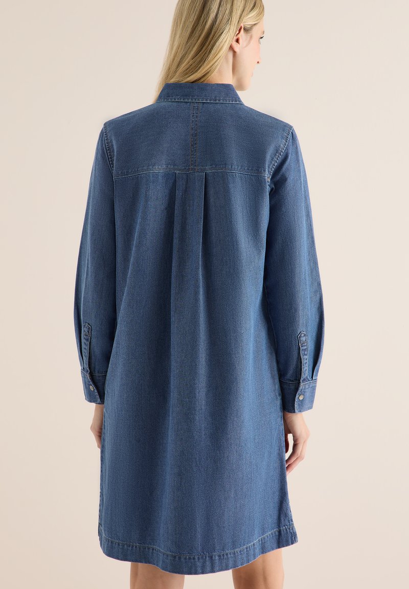 Denimklänning med lång ärm, blå färg, knappmanschetter och ryggveckdetalj. Slät textur, knälång design.