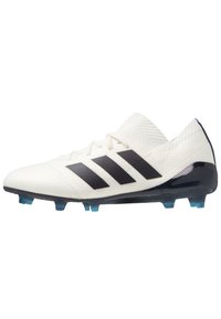 Botín de fútbol blanco con rayas negras de Adidas. Presenta una parte superior texturizada, un diseño de corte bajo y tacos transparentes azules sobre una suela negra.