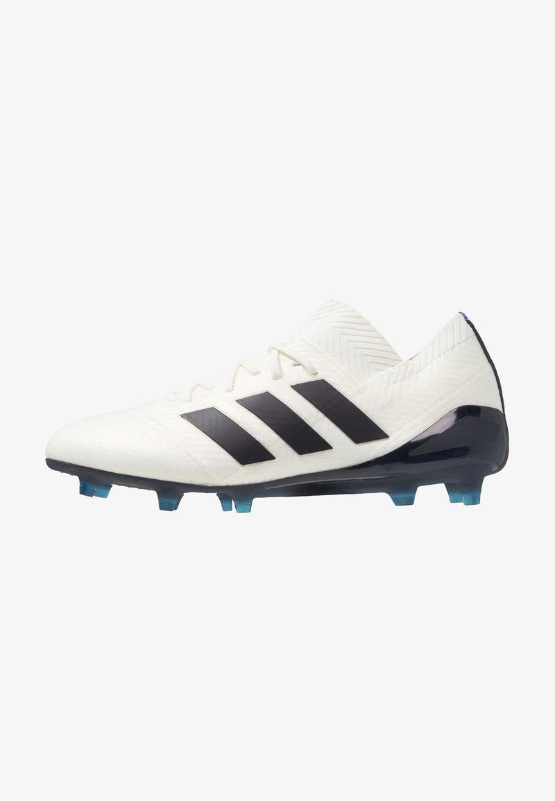 Botín de fútbol blanco con rayas negras de Adidas. Presenta una parte superior texturizada, un diseño de corte bajo y tacos transparentes azules sobre una suela negra.