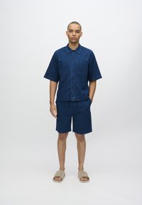 Farmering rövid ujjú ing, két mellzsebbel, megegyező farmer shorttal párosítva. Slim fit, sötétkék szín, sima textúra, laza stílus.