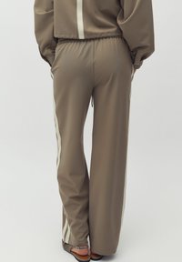 Beiga joggingsbyxor med lös passform, med vita sidostraps, ett elastiskt midjeband och en mjuk, lätt tekstur.