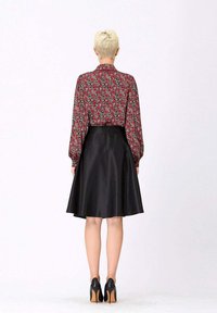 Blouse florale rouge à manches longues, associée à une jupe noire en satin évasée. La tenue présente une texture lisse et une taille cintrée. Talons noirs.