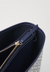 Interno di una borsa a tracolla in pelle blu navy, con una cerniera dorata, fodera in tessuto e un'etichetta con il marchio. Motivo geometrico sul tessuto esterno.