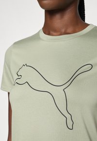 Olivi vihreä lyhythihainen t-paita pehmeästä kankaasta, jossa on suuri musta Puma-logo painettuna etupuolelle, pyöreällä pääntielle.