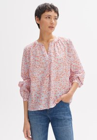 Blusa con motivo floreale in tonalità di rosa chiaro e arancione, con una vestibilità ampia, scollatura a V e dettagli arricciati sulle spalle. Maniche lunghe.