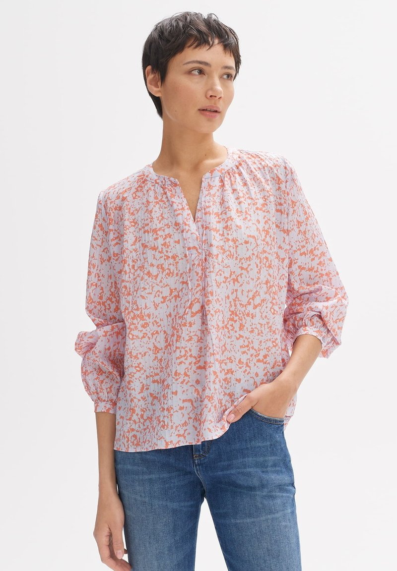 Blusa con motivo floreale in tonalità di rosa chiaro e arancione, con una vestibilità ampia, scollatura a V e dettagli arricciati sulle spalle. Maniche lunghe.